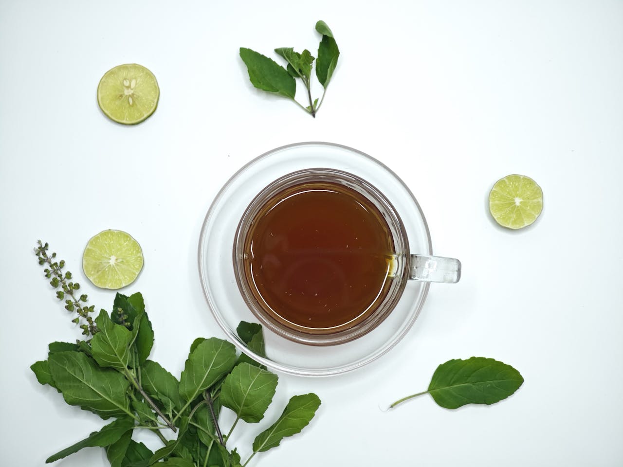 A cup of aromatic tulsi tea surrounded by fresh lime slices and basil leaves, offering a refreshing herbal beverage.